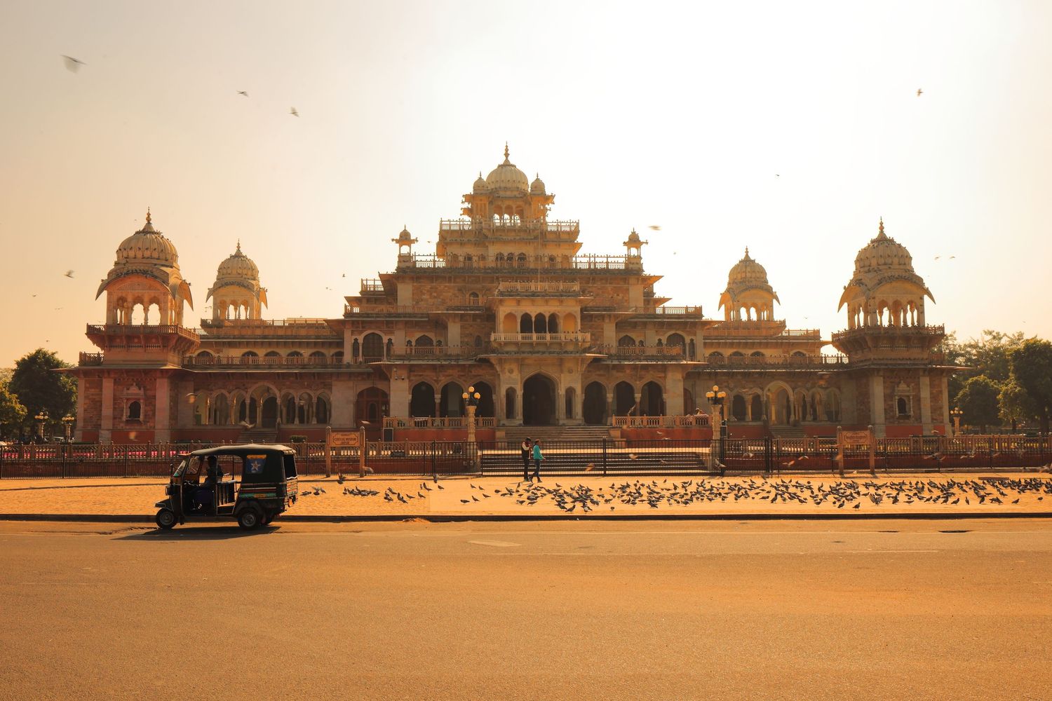 Albert Hall Museum in Jaipur glowing at sunset with auto rickshaw in foreground.
