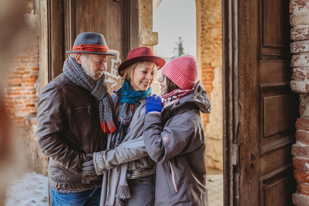 Three individuals in warm winter attire gathered closely in a brick doorframe.