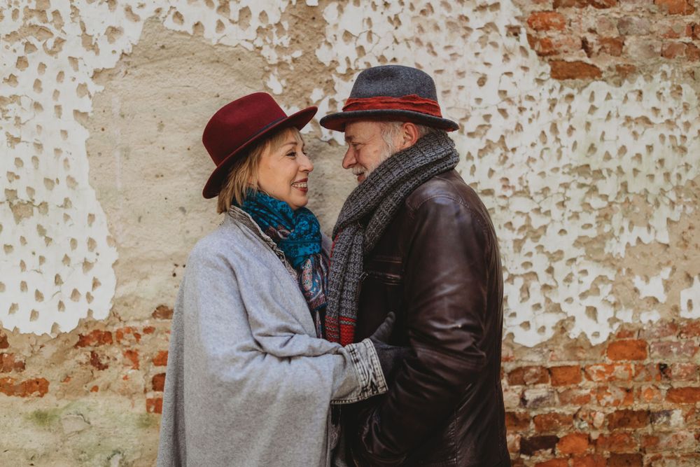 Two people in winter hats sharing an intimate moment against weathered brick wall.