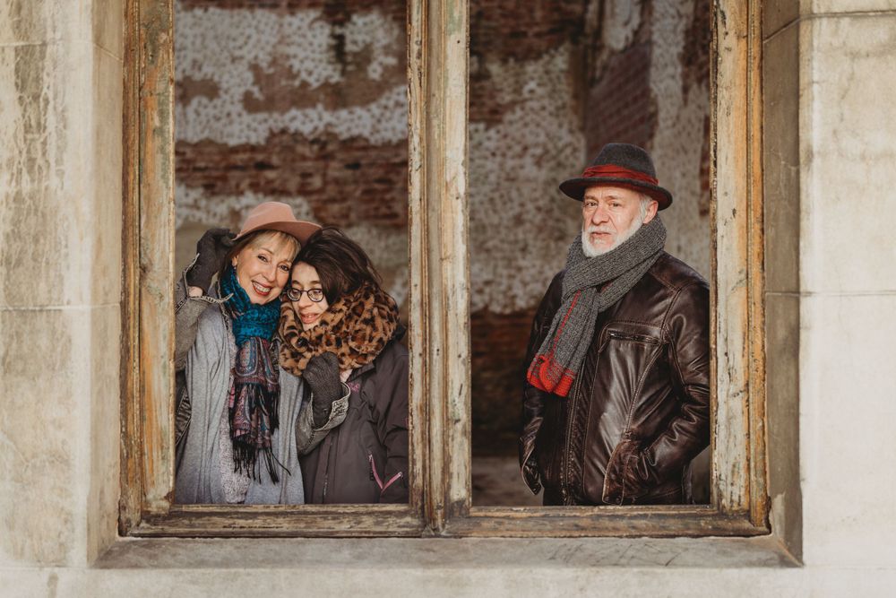 Three people framed within a weathered window of an old brick building.