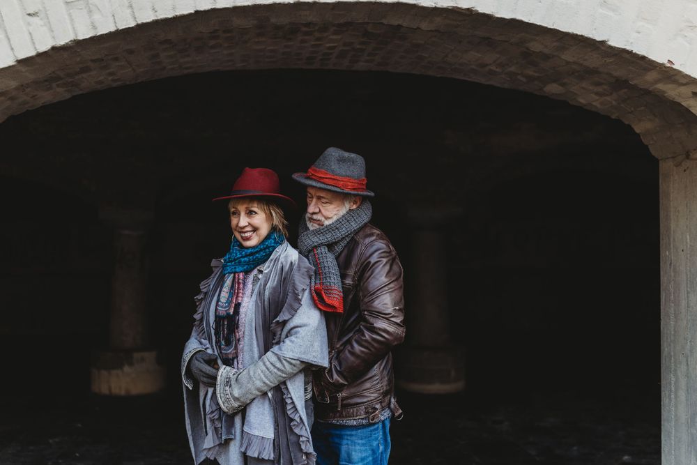 A couple in matching red hats and winter coats pose together under a stone archway.