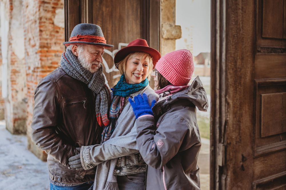 Group of three people in winter clothing embracing in a doorway with brick walls.