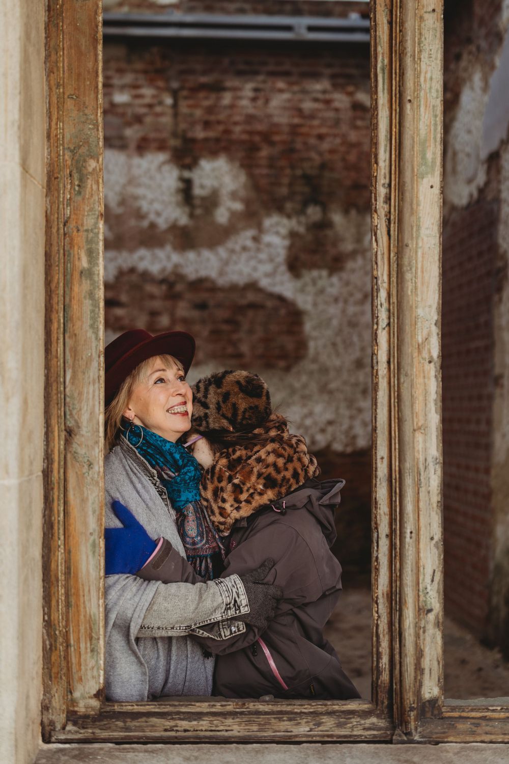 Two people sharing a moment through an old window frame with exposed brick background.