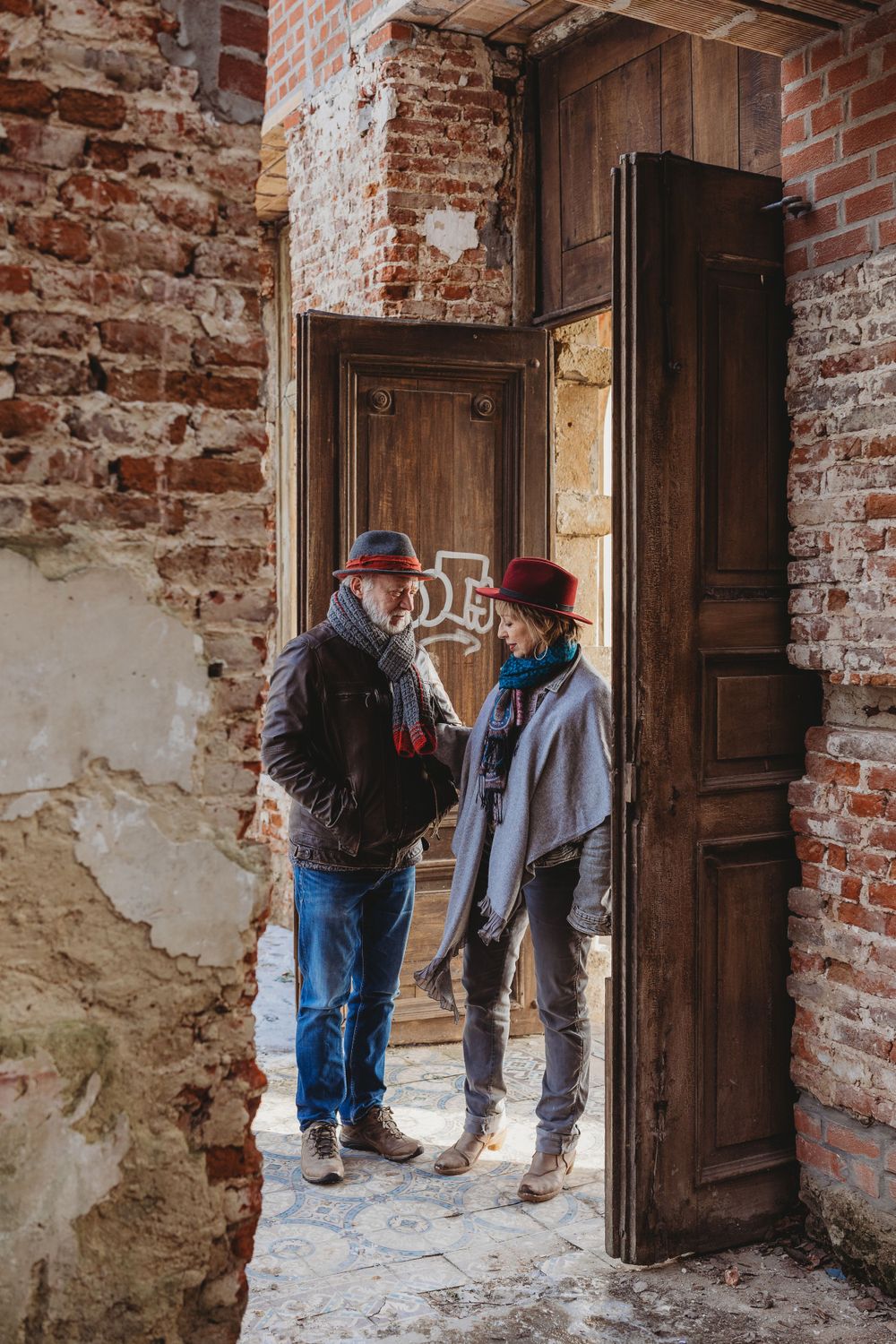 Two people having a conversation in a rustic doorway with exposed brick walls.