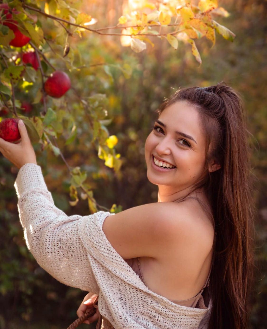 Woman posing for a portrait picking apples in the autumn sun