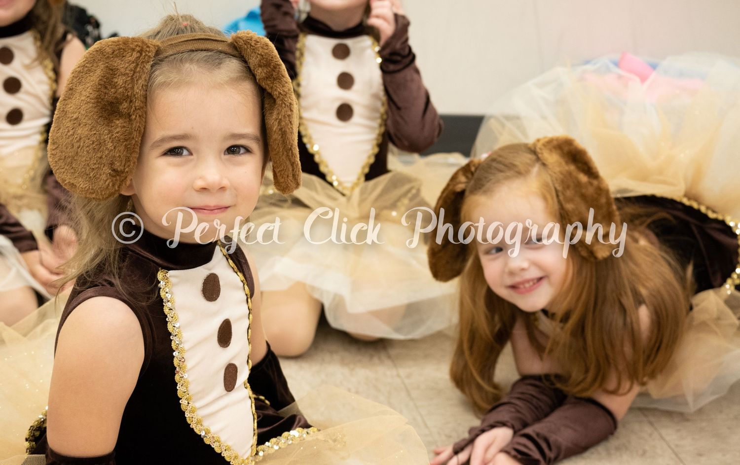 Two young dancers in recital costumes with mouse ears lay on studio floor during dance performance.