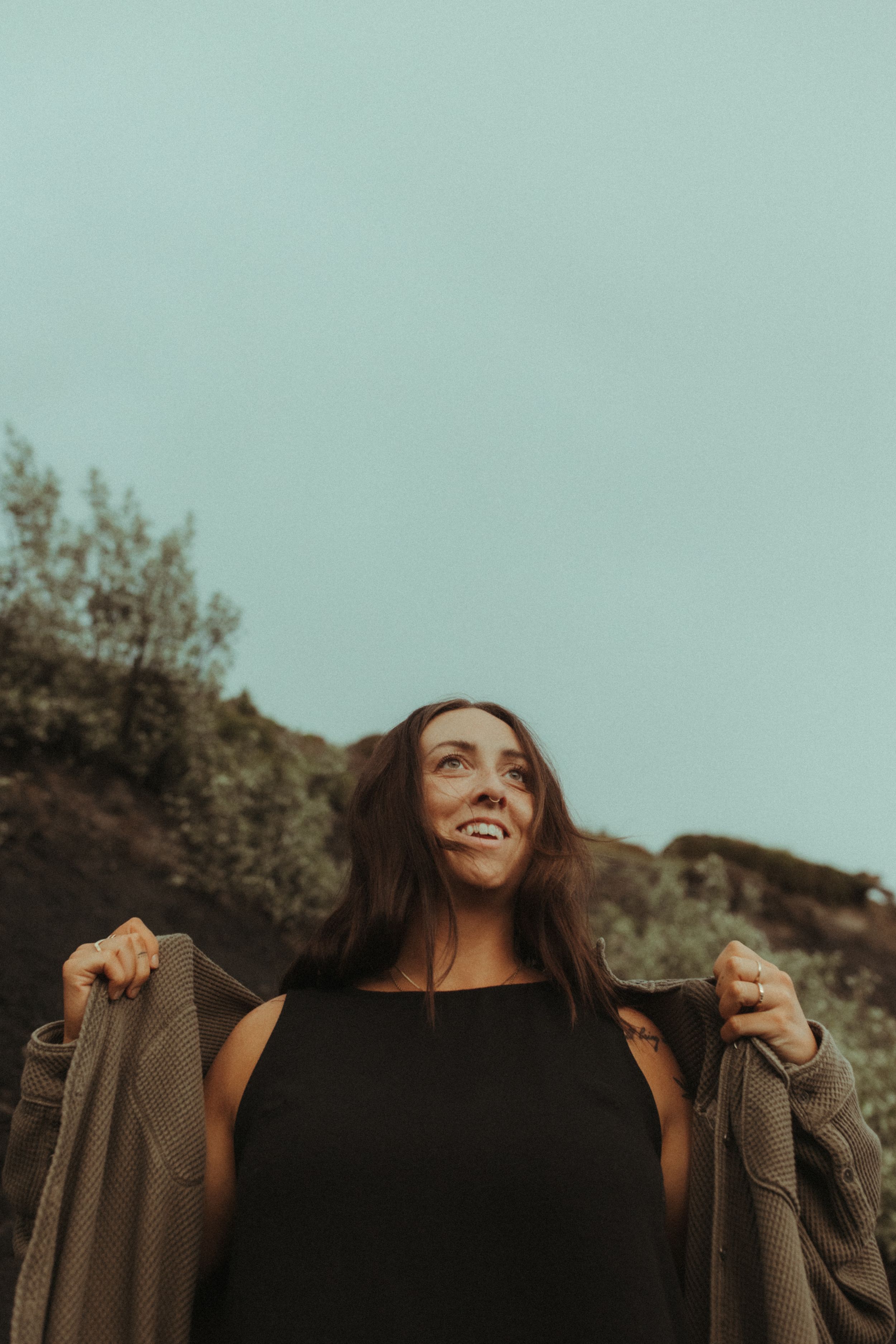 Portrait of a woman in a black top and cardigan against a natural backdrop.