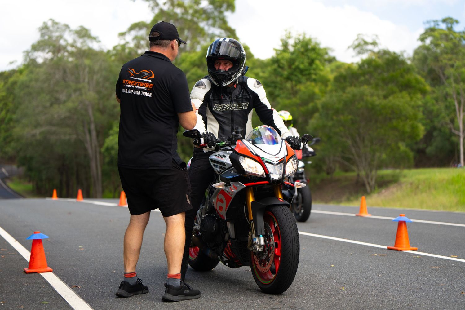 Motorcycle training session with instructor and student on track with safety cones.
