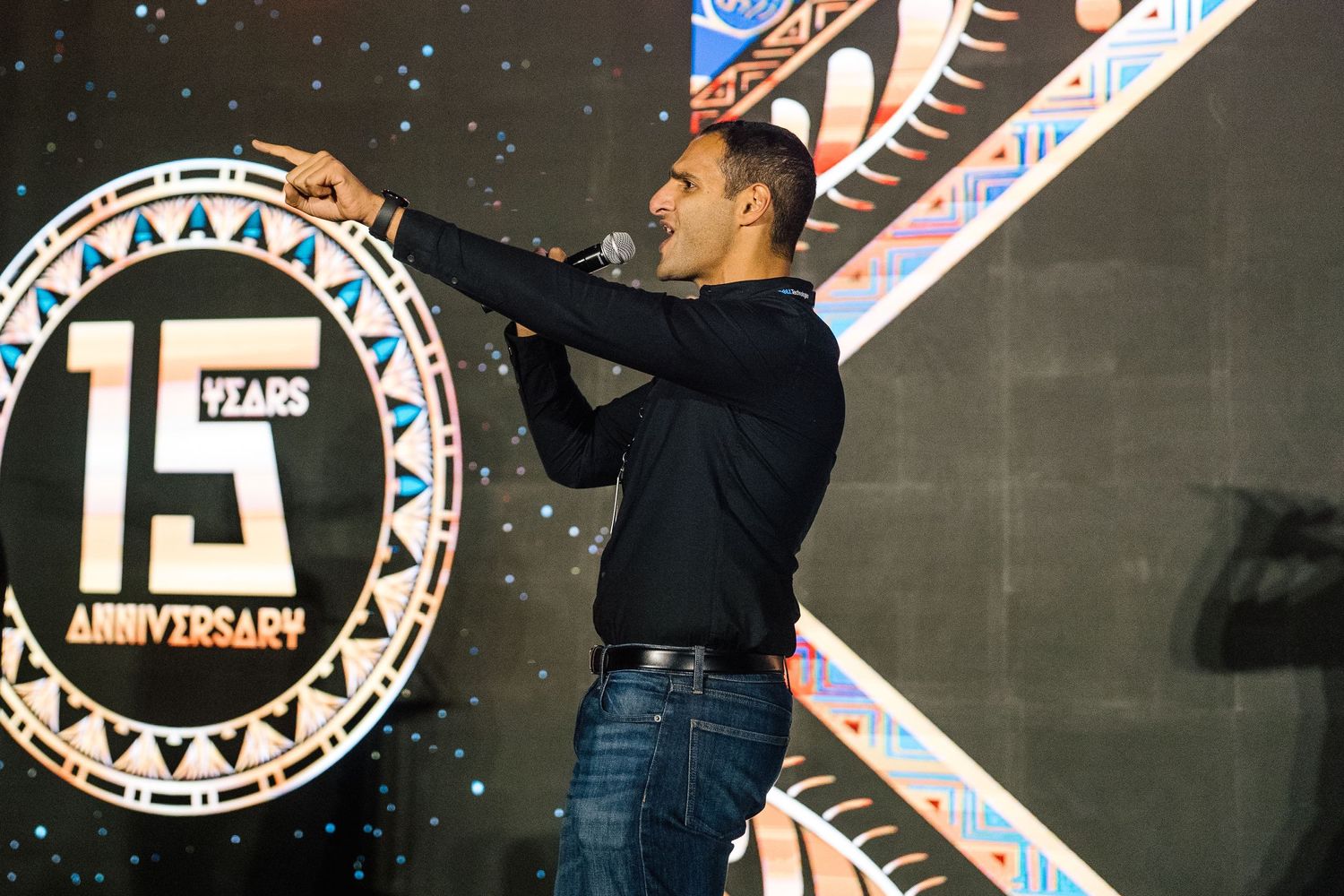 Person on stage gesturing during a 15th anniversary celebration event.