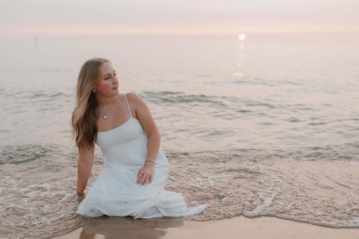 A person in a white dress poses at sunset by the ocean.