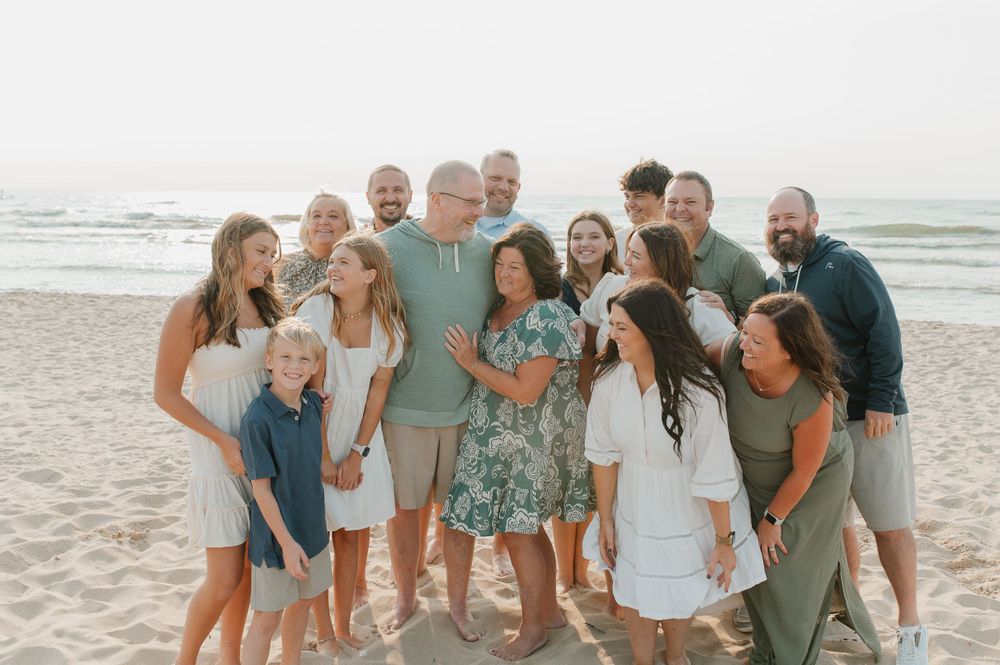 Family members share candid laughs during a beach photoshoot in coordinated casual outfits.