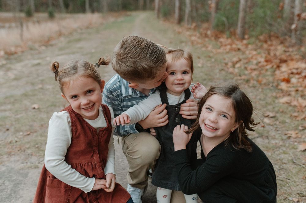 A playful outdoor family photo showing four people laughing together on a fall day.