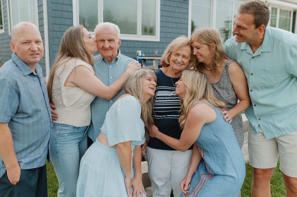 Extended family posing together outside a blue house for a casual group photo.