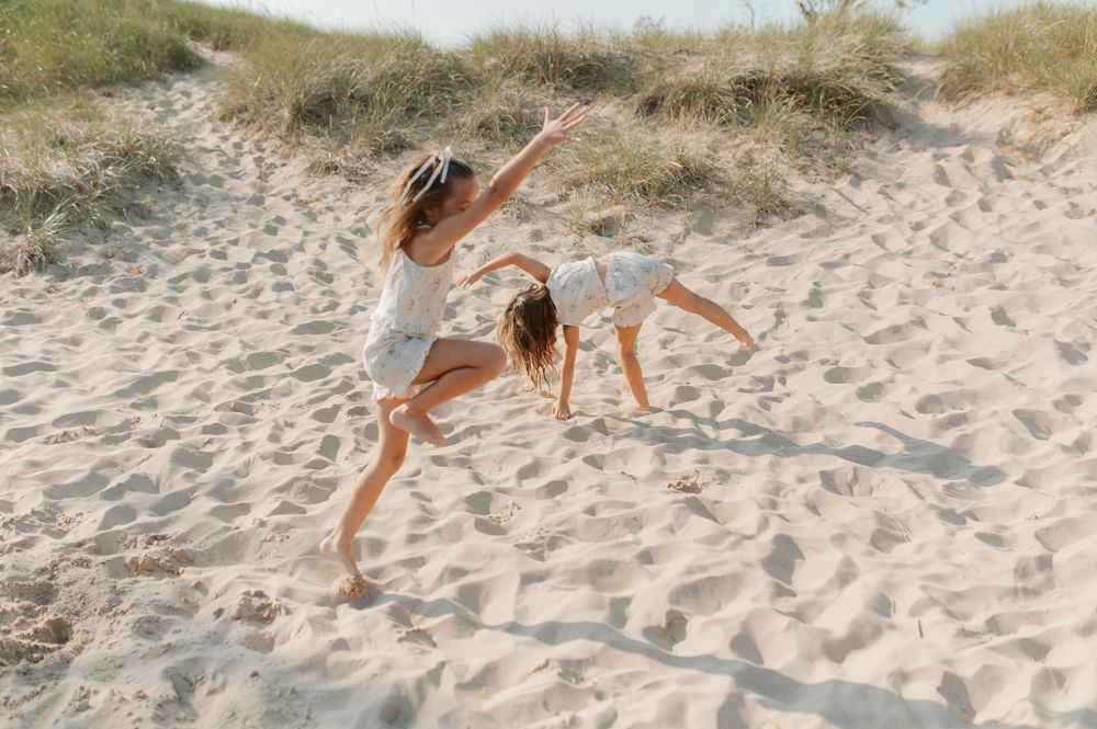 Two figures leap joyfully in the air on sandy dunes during a summer photoshoot.