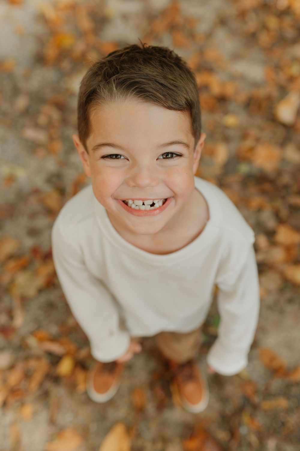 An overhead portrait of a child in a cream sweater smiling broadly at the camera.