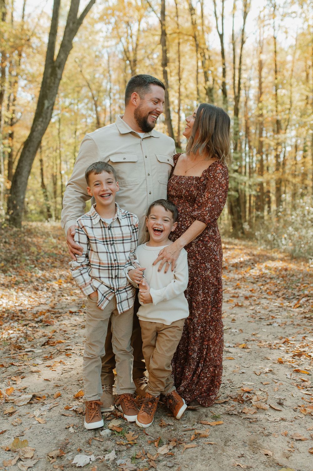 A family of four laughing together on an autumn path covered in fallen leaves.