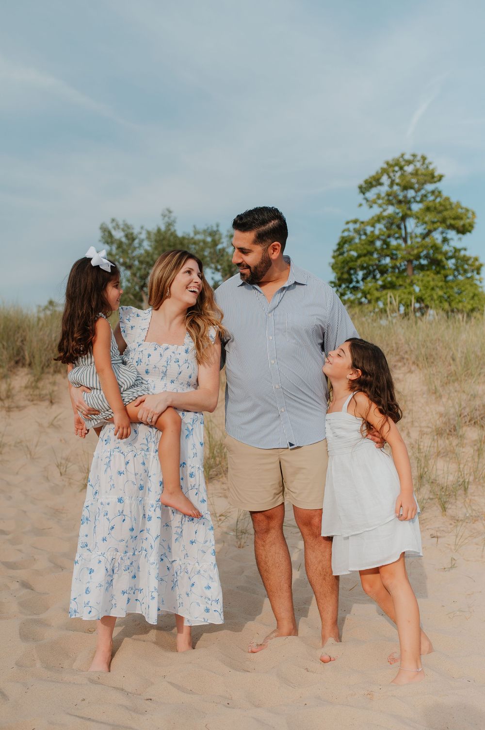 Family shares joyful moments together while posing on sandy dunes in coordinated outfits.