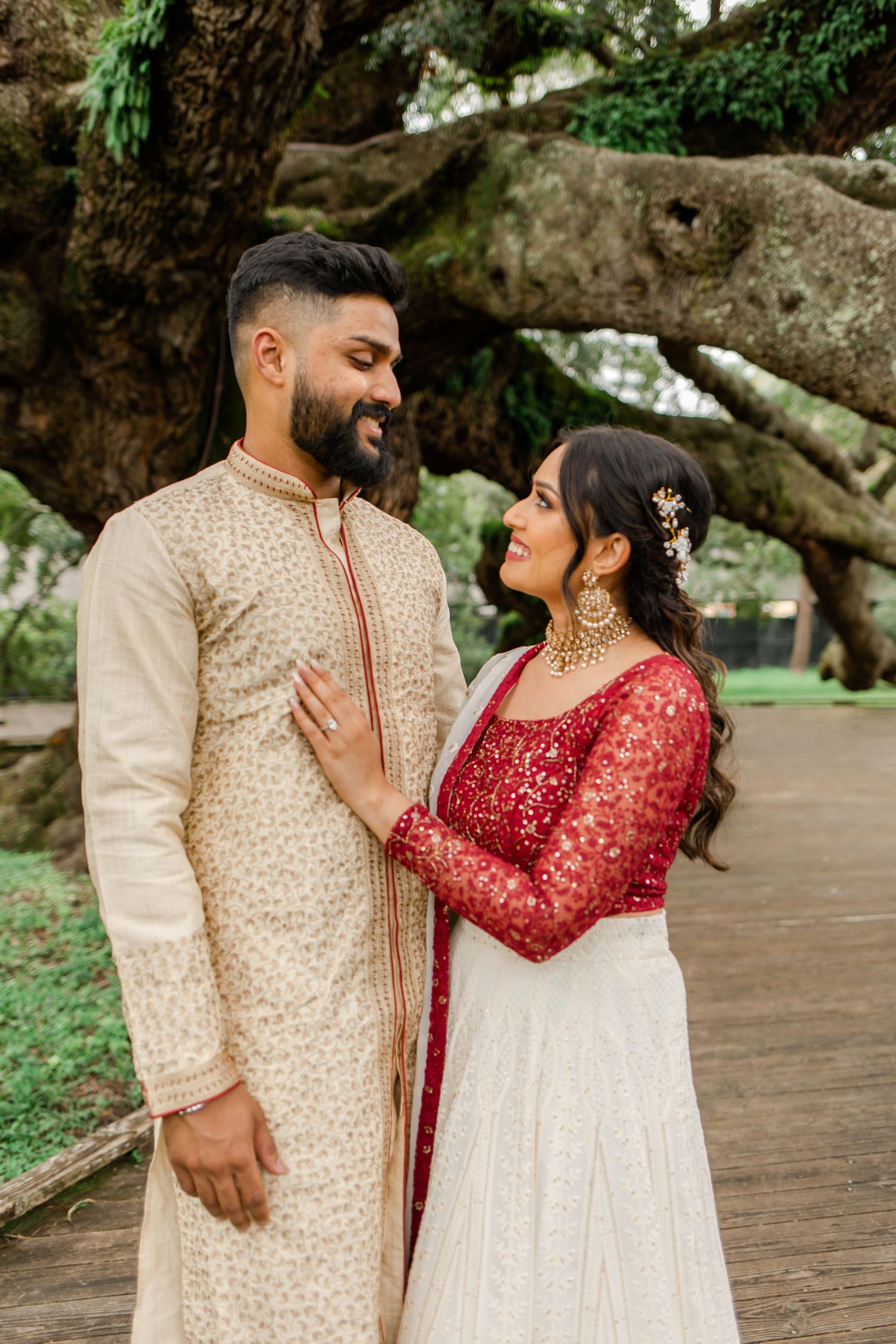 A couple in traditional South Asian wedding attire share intimate moments in a garden setting.