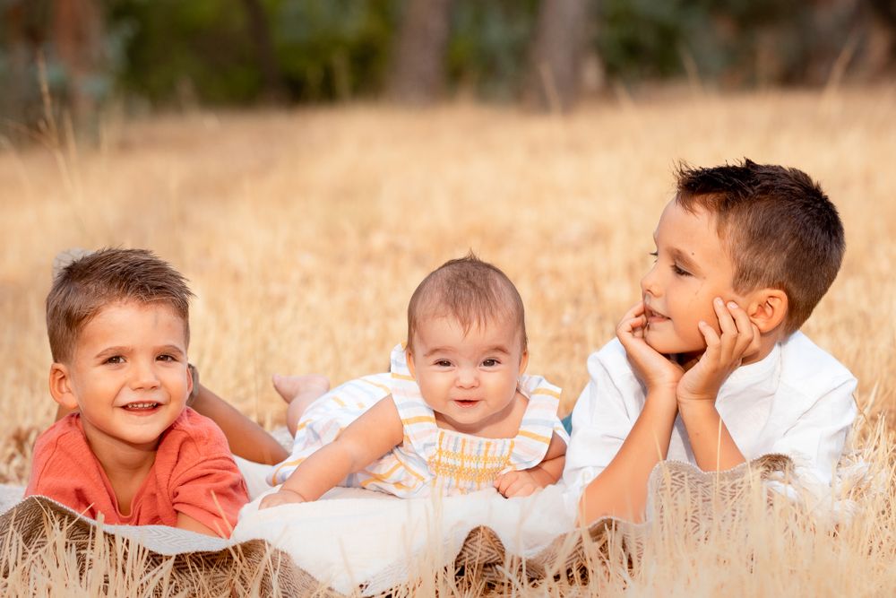 Children lying in tall grass during sunset for outdoor family photos.