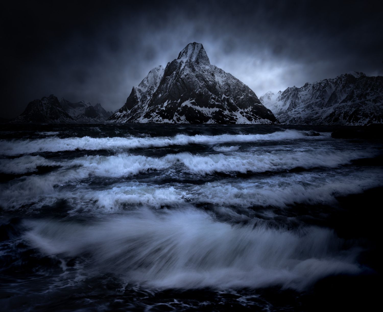 Dramatic mountain peak under dark stormy clouds with rushing water in the foreground.