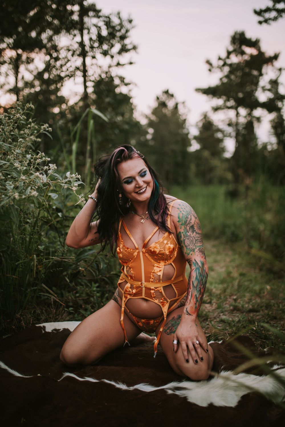 Boudoir photography in an orange lingerie set against a natural forest backdrop at sunset.