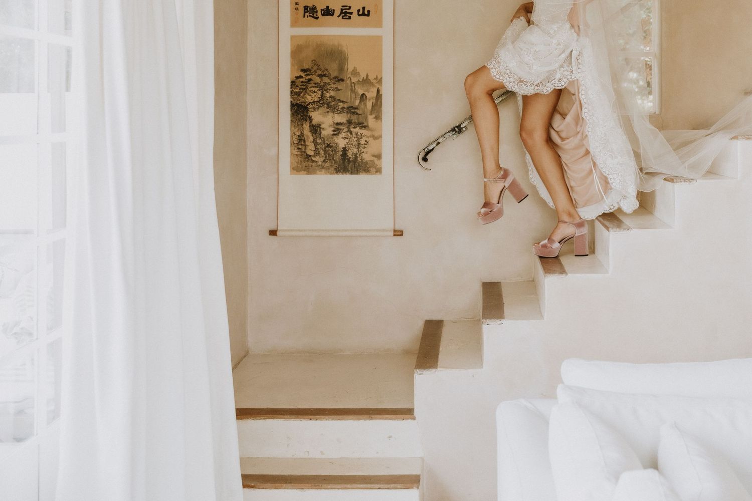 Elegant bridal shoes and dress details on white stairs with Asian artwork on the wall.