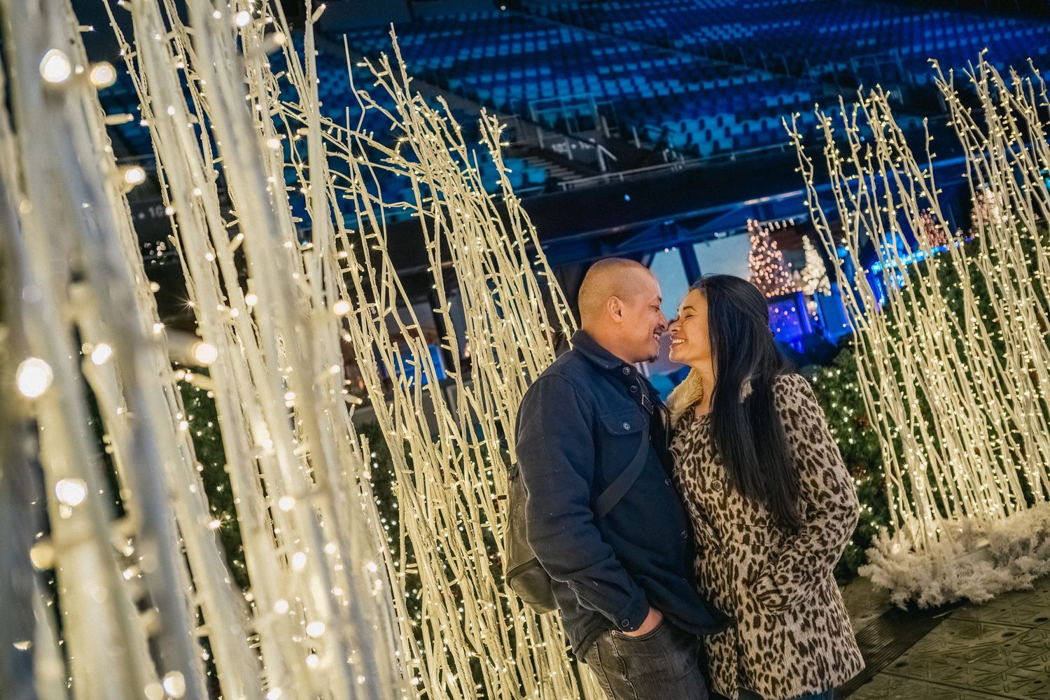 A romantic moment among illuminated white branches and blue lighting at a holiday display.