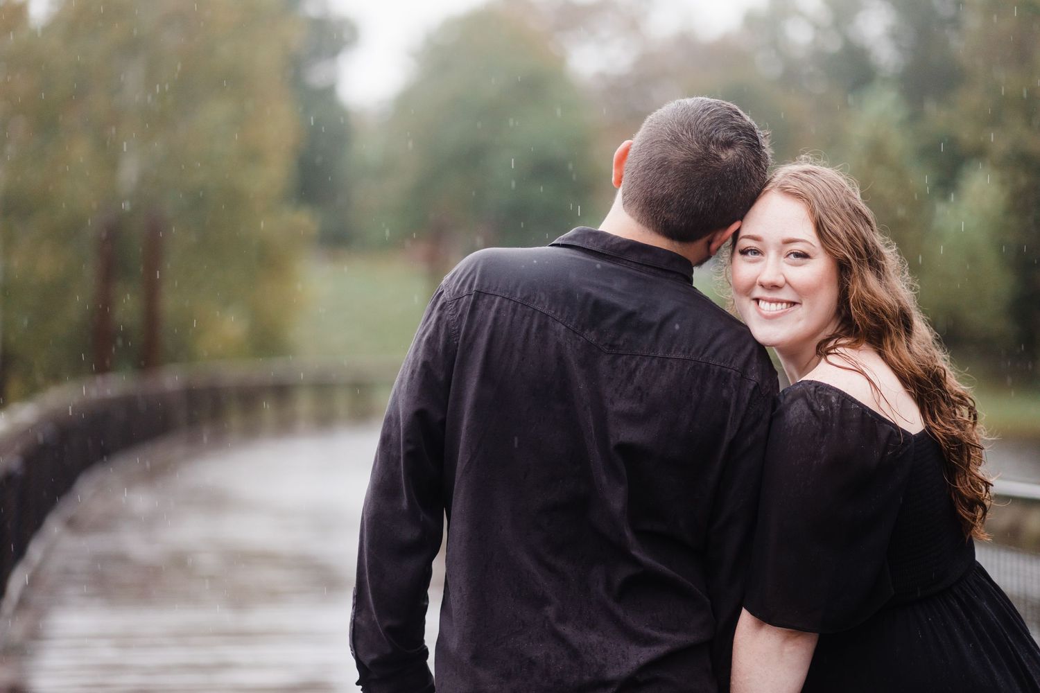 Couple in dark clothing embracing by lakeside on cloudy autumn afternoon.