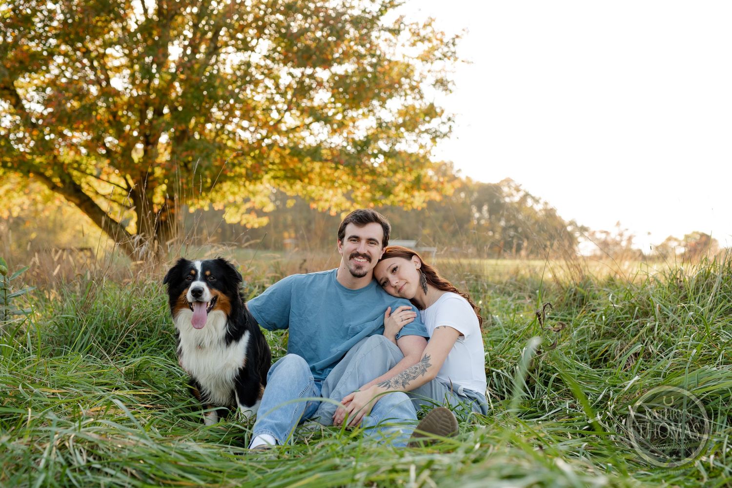 A couple and their Border Collie dog relax together in a grassy field during golden hour sunset.