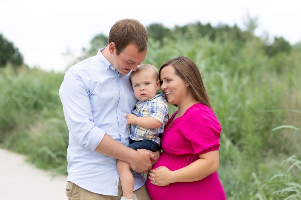 A mom and dad hug their baby boy while mom holds her baby bump.