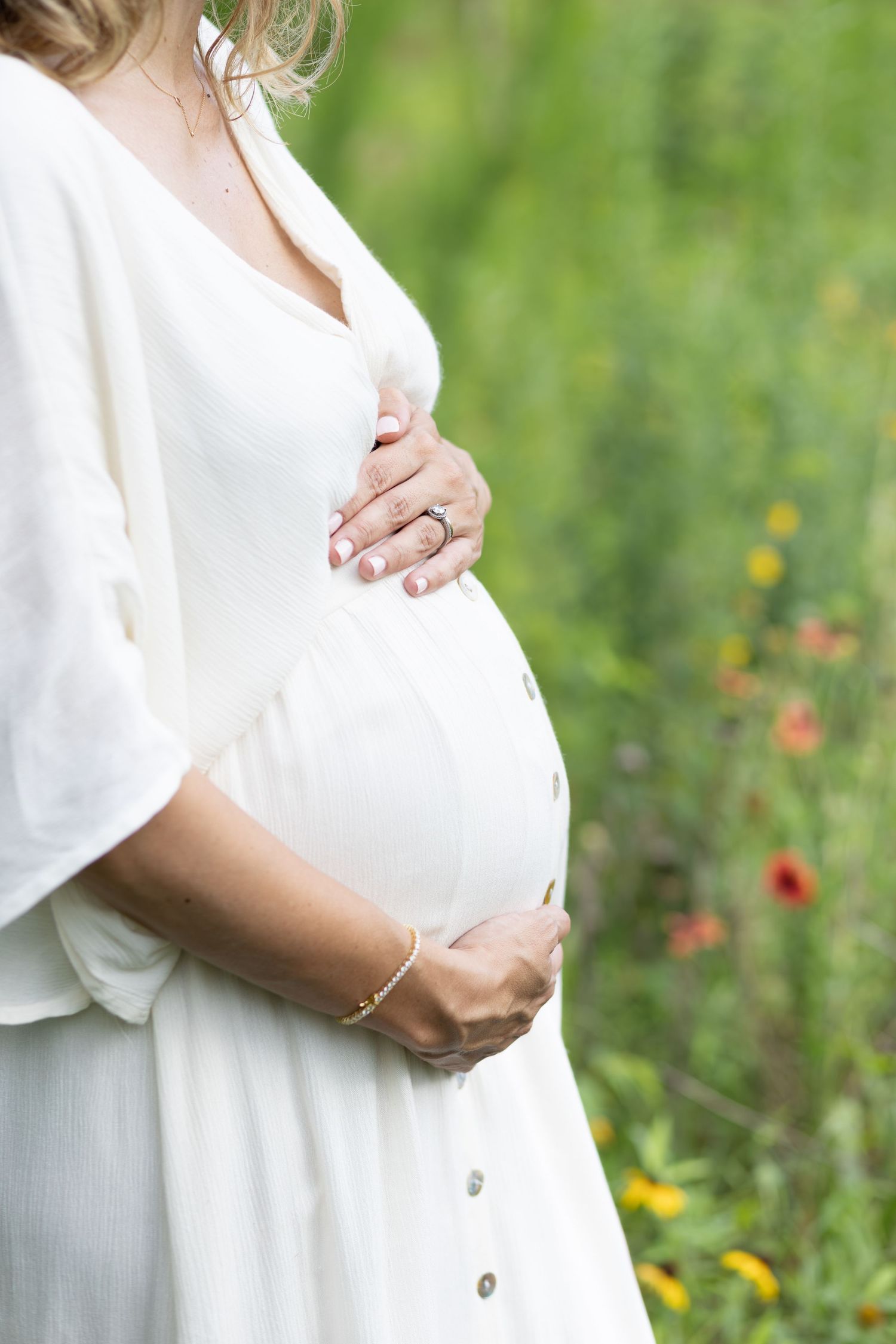 A Raleigh, NC wildflower maternity session. A woman holds her bump in a dress in a field of flowers.