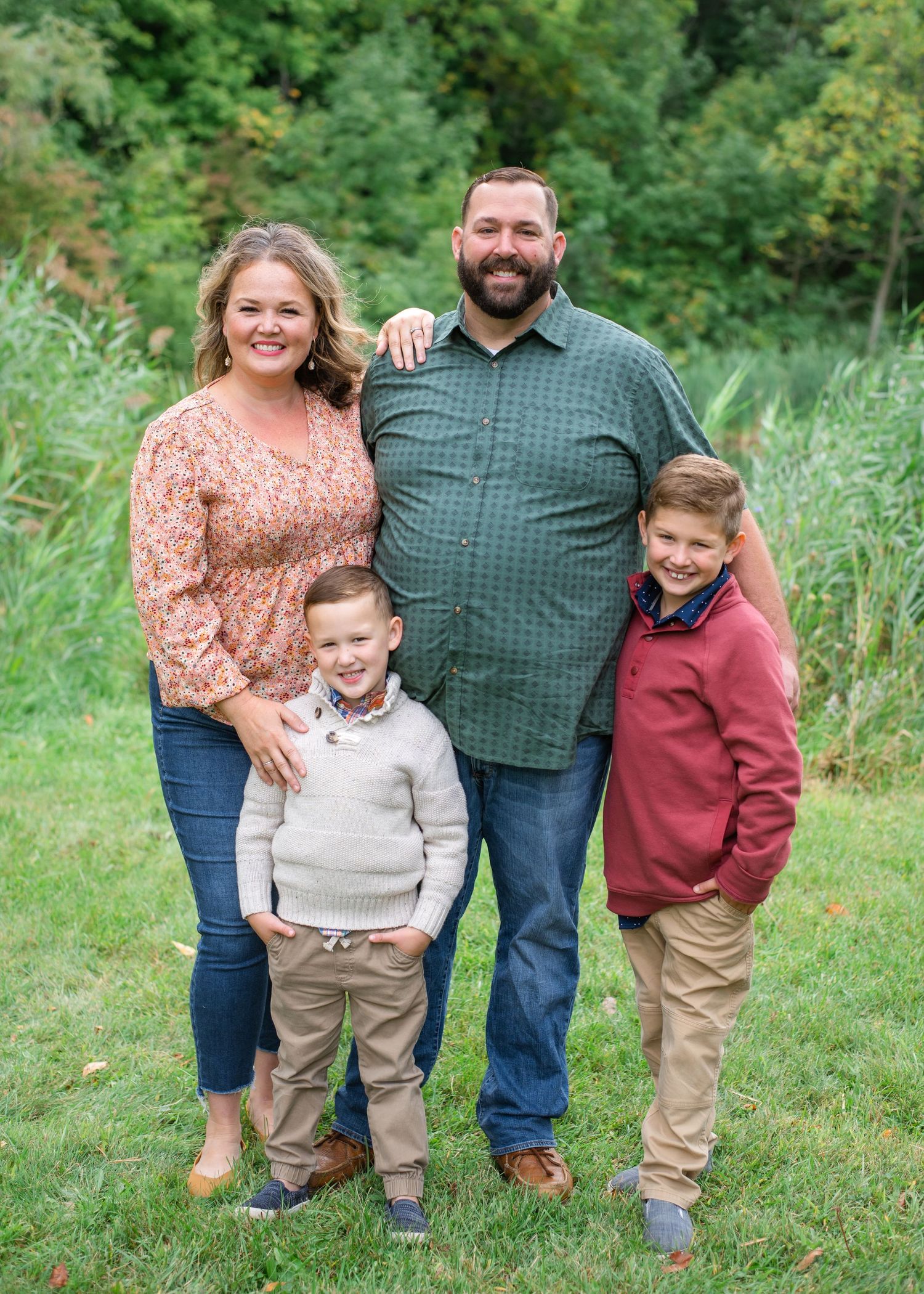 A casual family portrait taken outdoors against a lush green summer background.