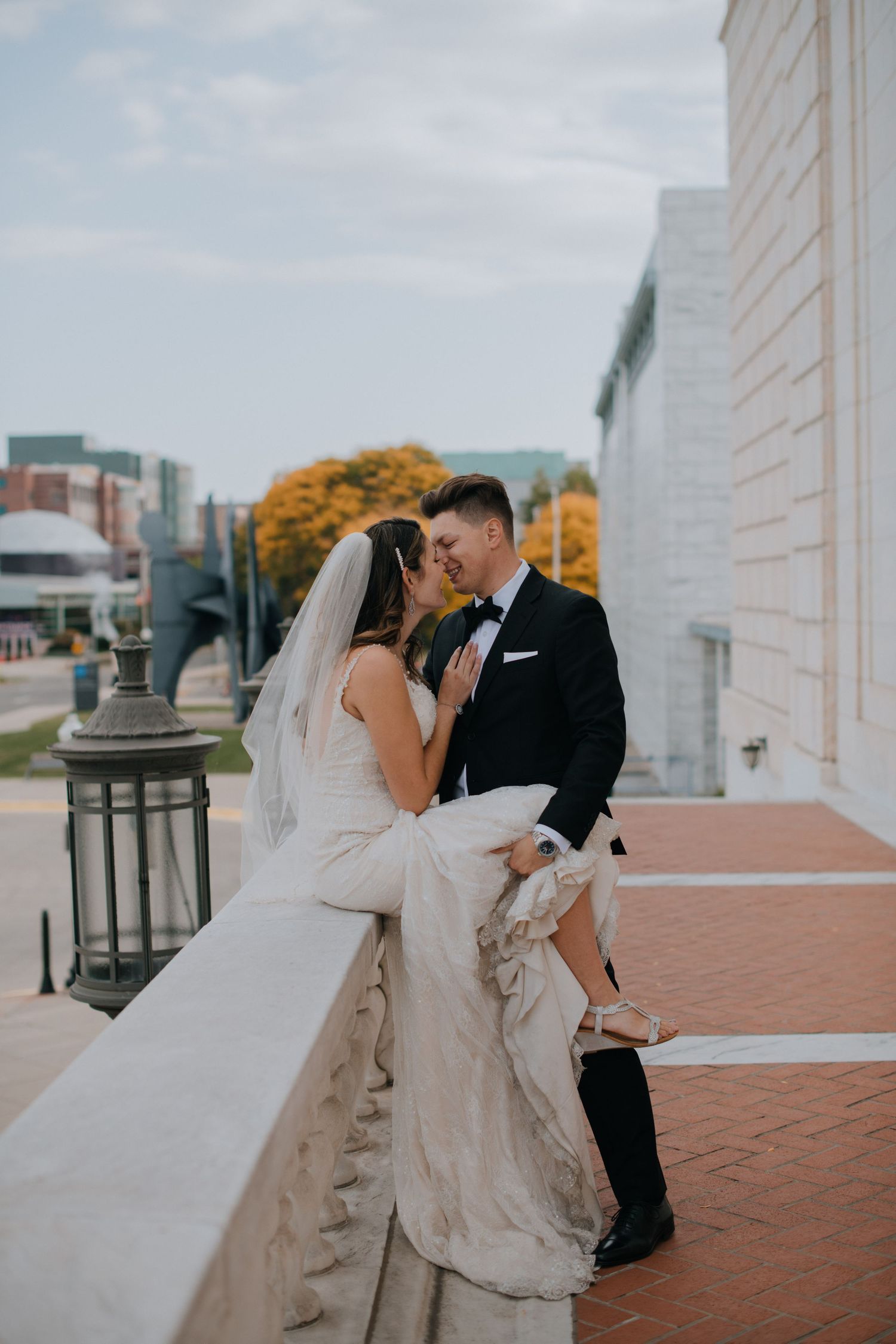 Romantic wedding couple shares an intimate moment on a terrace with autumn foliage in the background in Detroit wedding photography