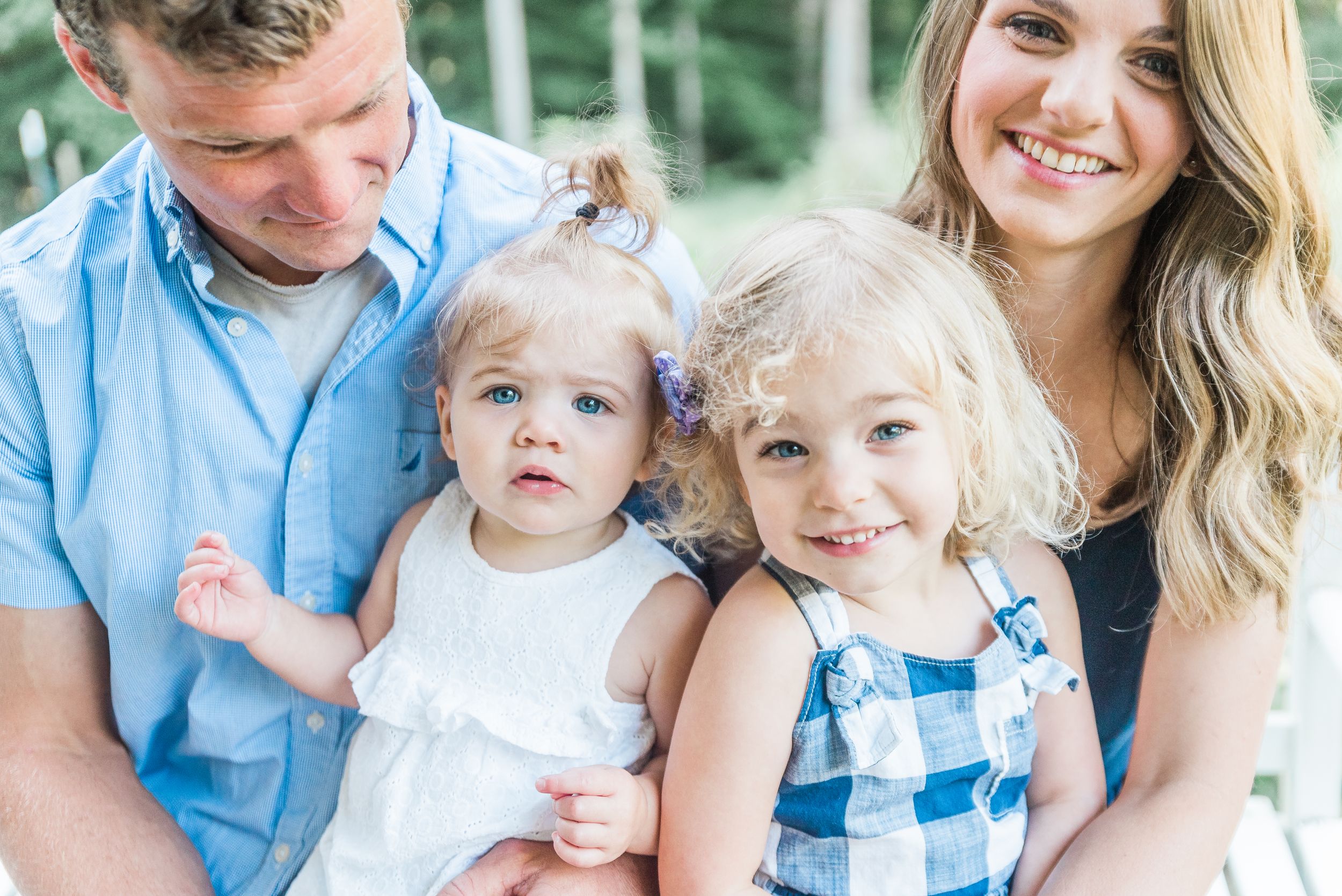 A family wearing coordinated blue and white outfits poses together outdoors for a casual portrait session.