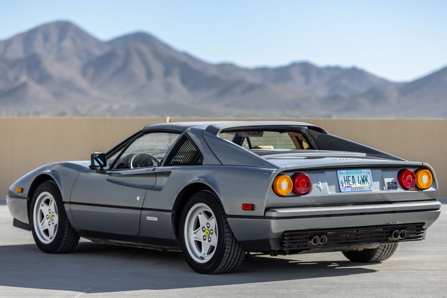 Vintage grey Ferrari 328 photographed in desert setting with mountains in background.