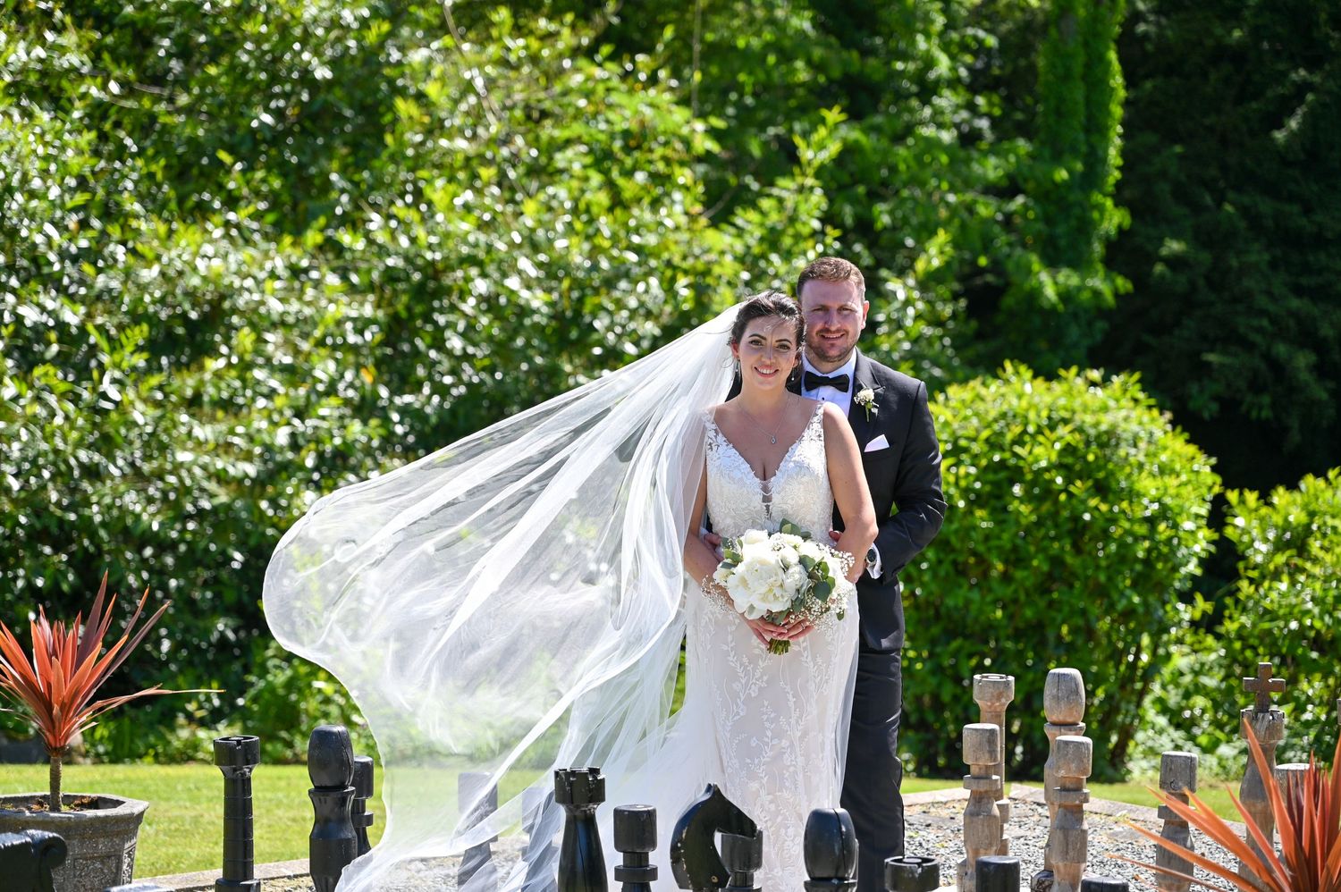 A bride in white with flowing veil poses outdoors while her dress catches the breeze.