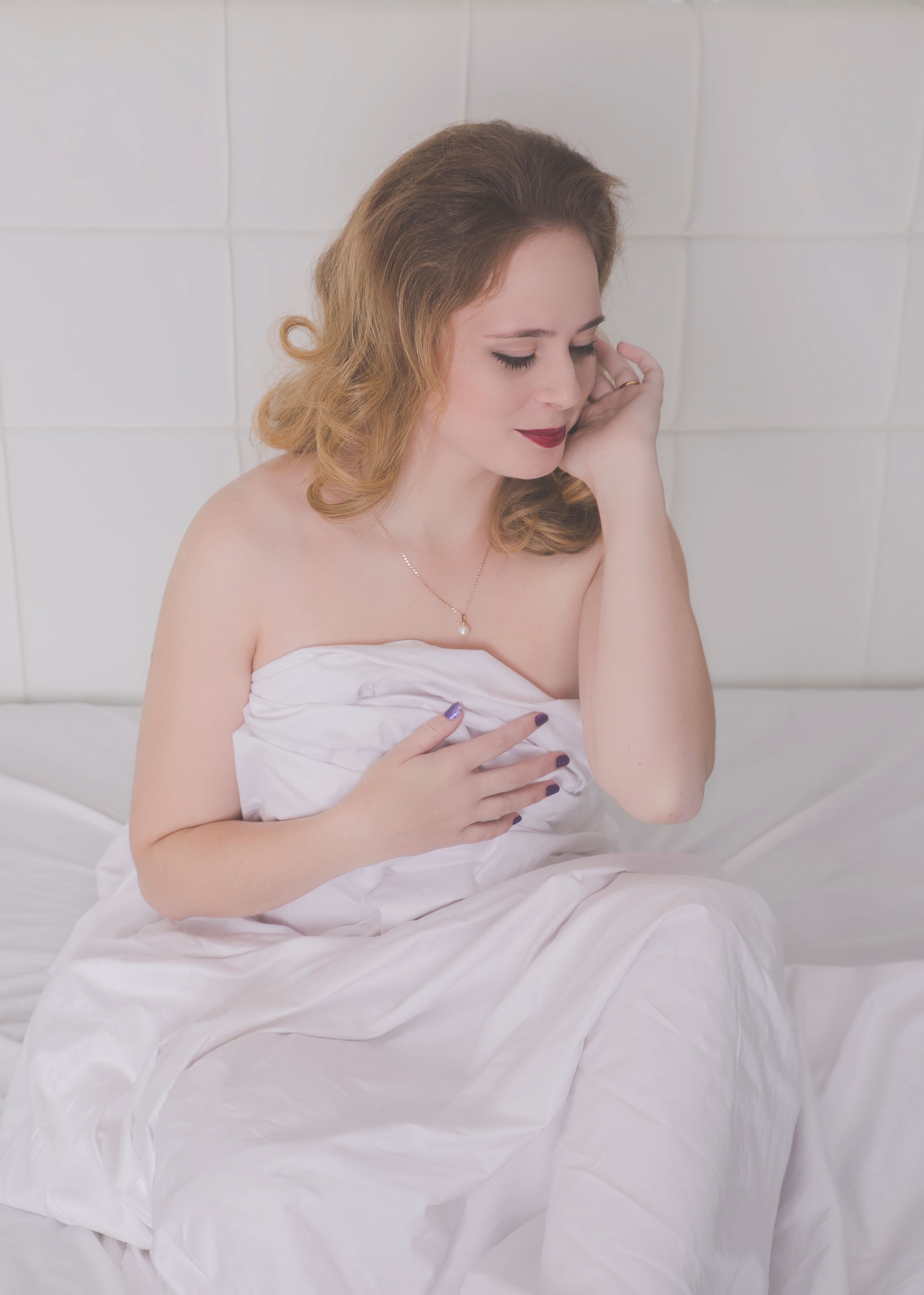 Intimate portrait wrapped in white bedding with soft natural lighting.