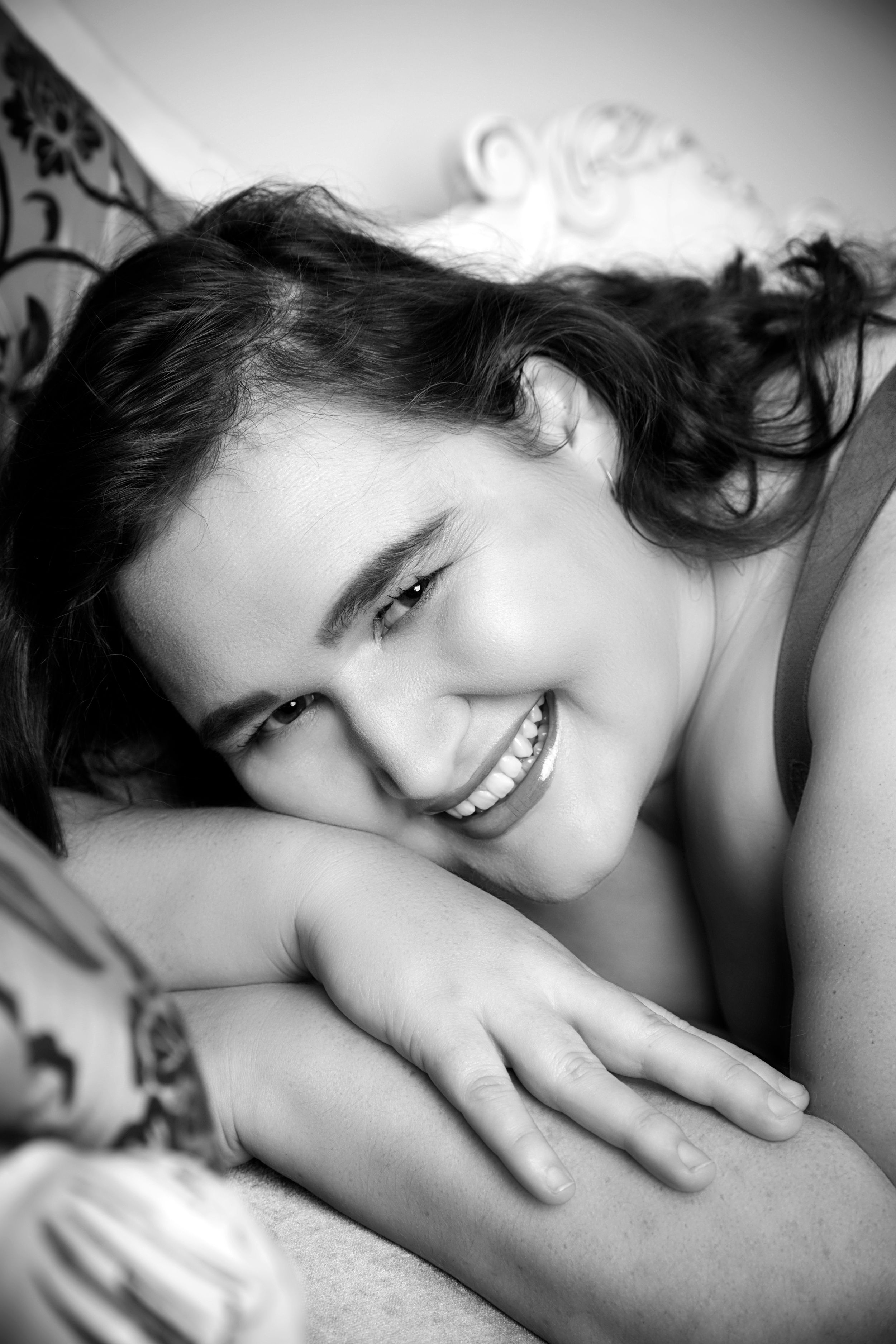 Artistic black and white portrait of a person with dark hair lying down against light bedding.