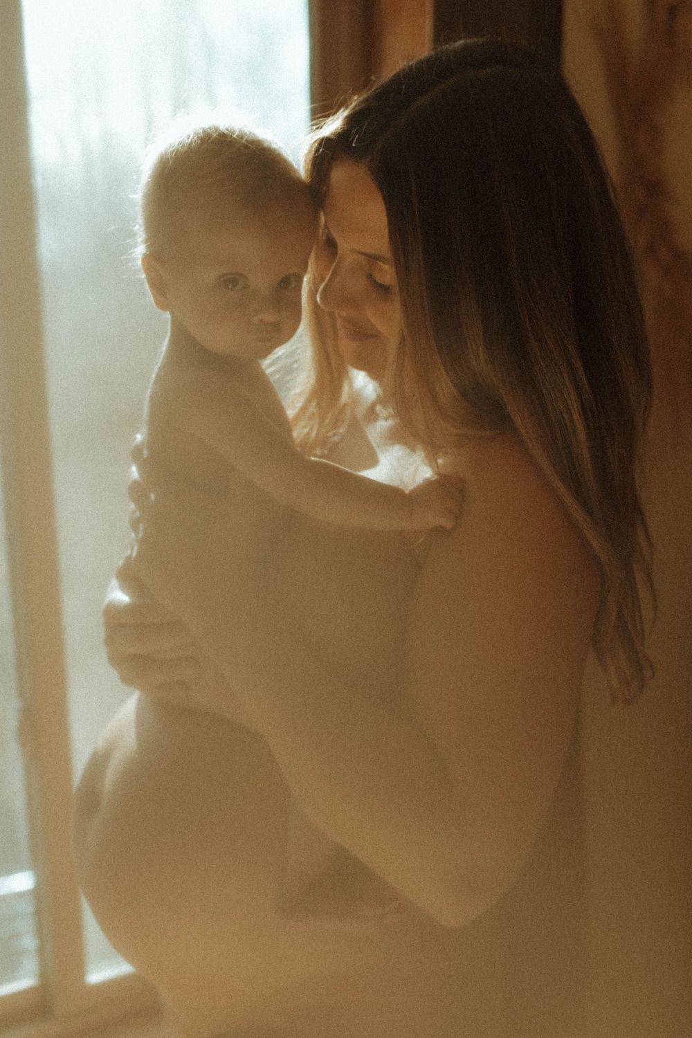 A tender moment between parent and baby bathed in soft window light.