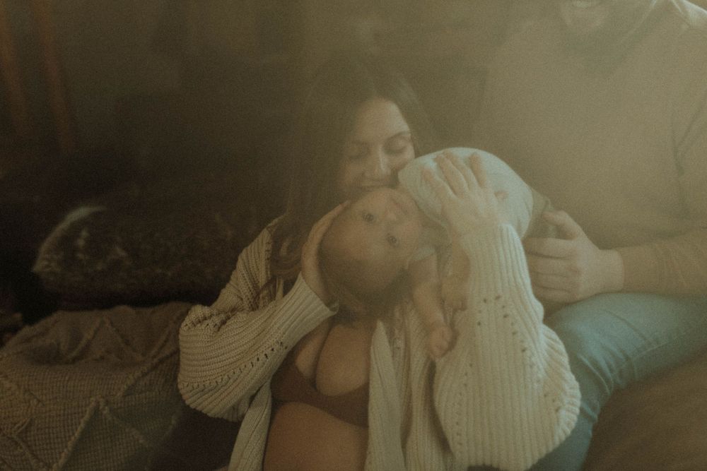 An intimate family cuddle moment on a brown leather sofa in soft atmospheric lighting.