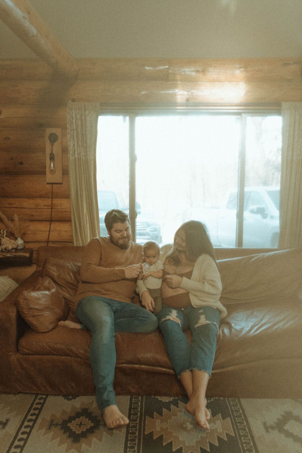 Family sharing tender moment together on couch in rustic cabin setting.