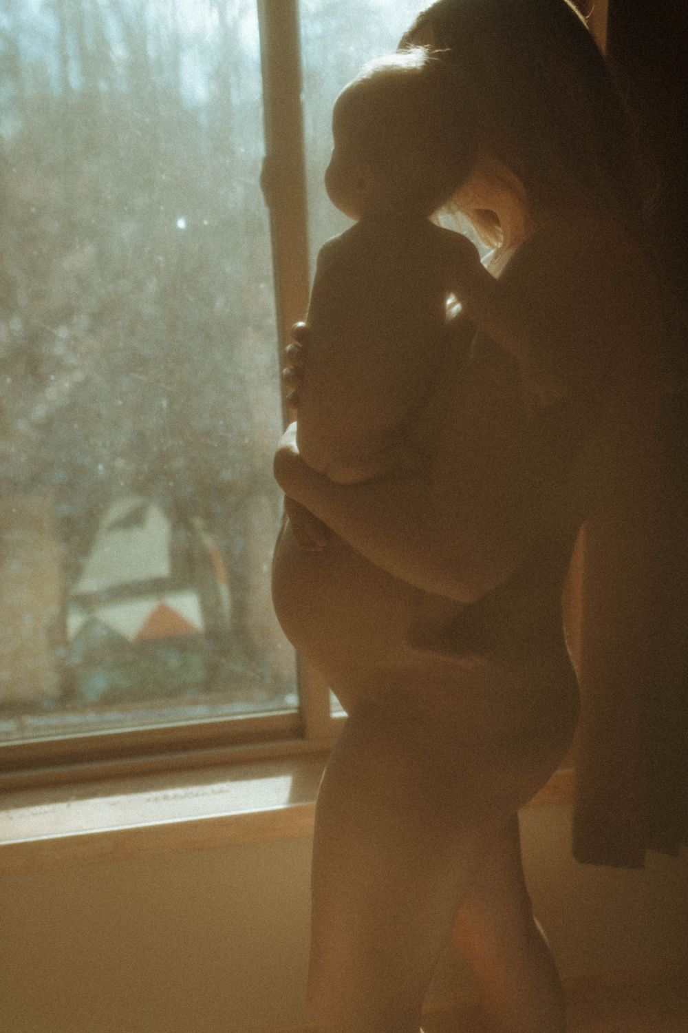 A silhouetted figure stands by a window in gentle morning light.