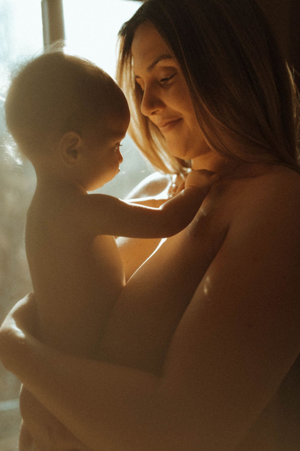 A warm backlit portrait showing intimate connection between parent and infant.