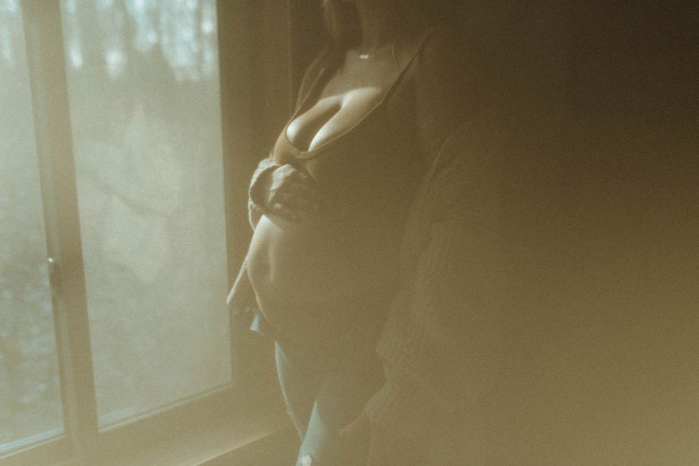 Silhouette against window with soft natural light in sepia tones creating moody atmosphere.