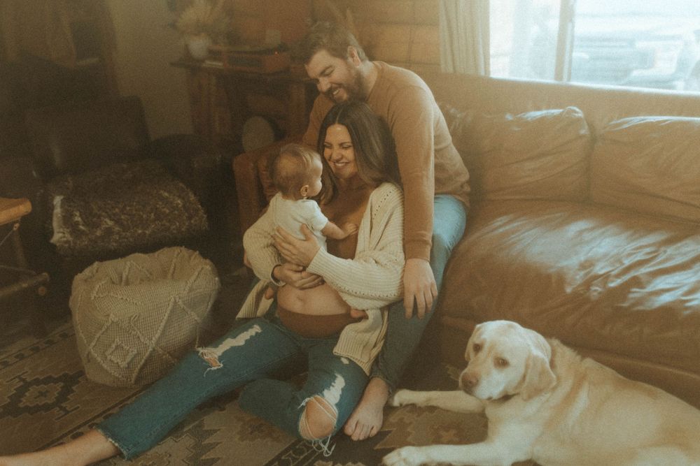 A heartwarming family scene with their white Labrador dog resting beside them on a leather couch.
