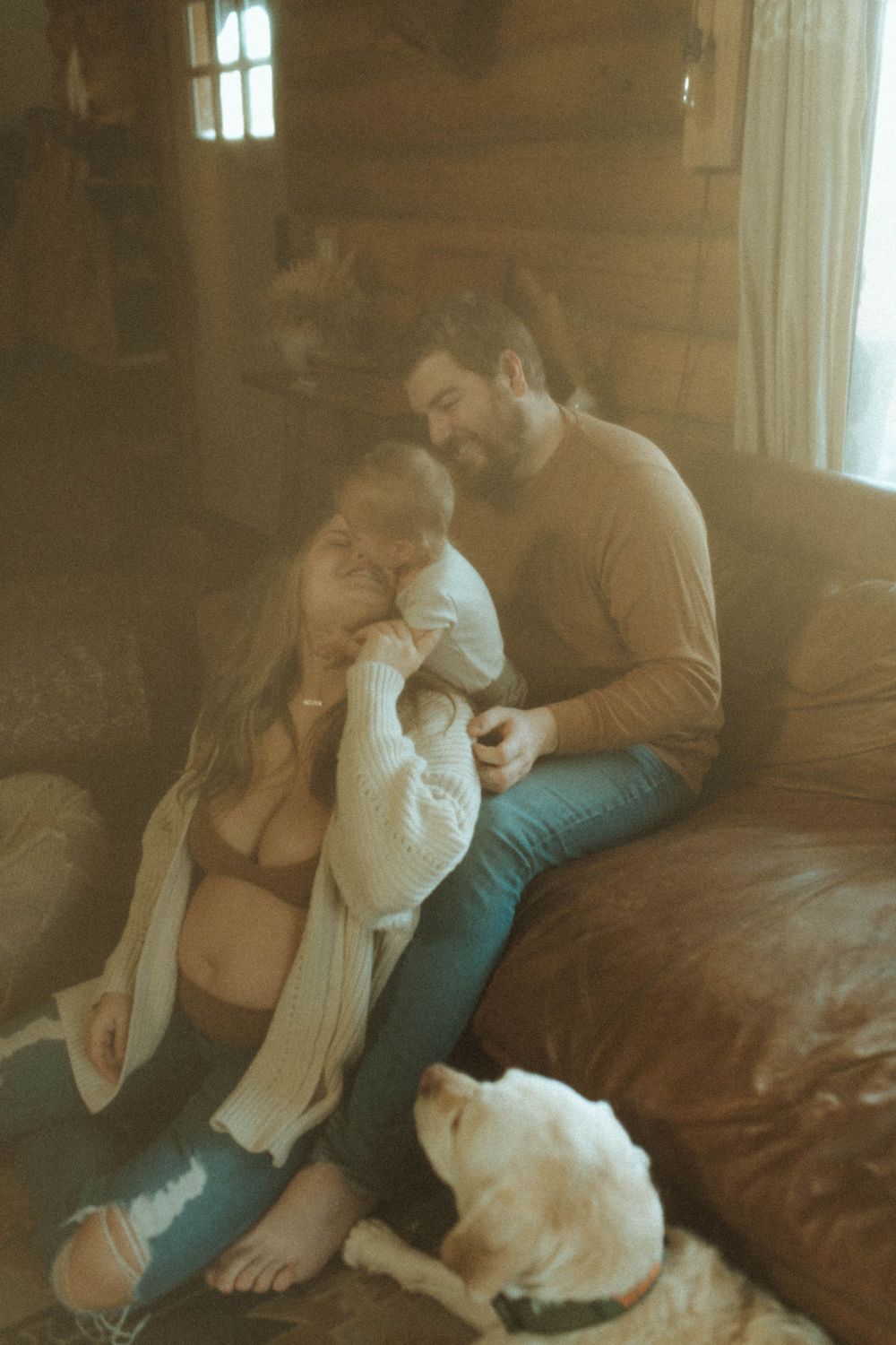 A cozy family moment on a leather couch with a white dog lying nearby in warm natural lighting.