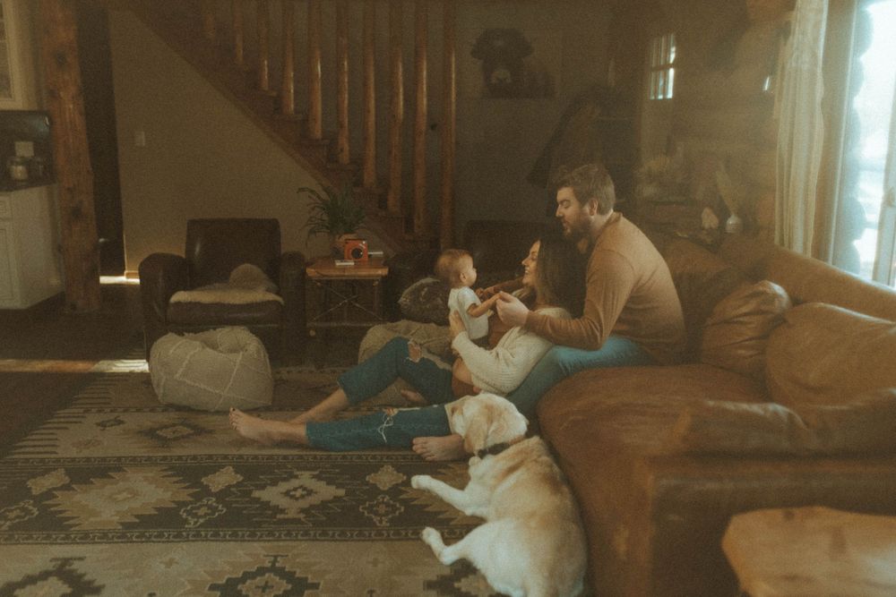 A family relaxing at home with their white dog on a patterned rug near wooden stairs.