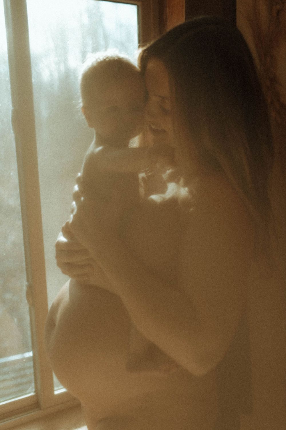 A gentle moment captured in warm light by a window with soft silhouettes.