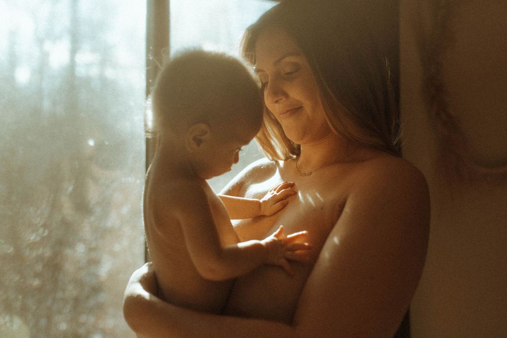 A sunlit intimate moment between parent and baby by a window.