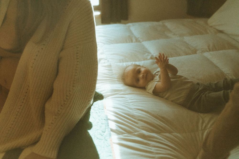 Small baby lying on white bedding in soft vintage lighting.